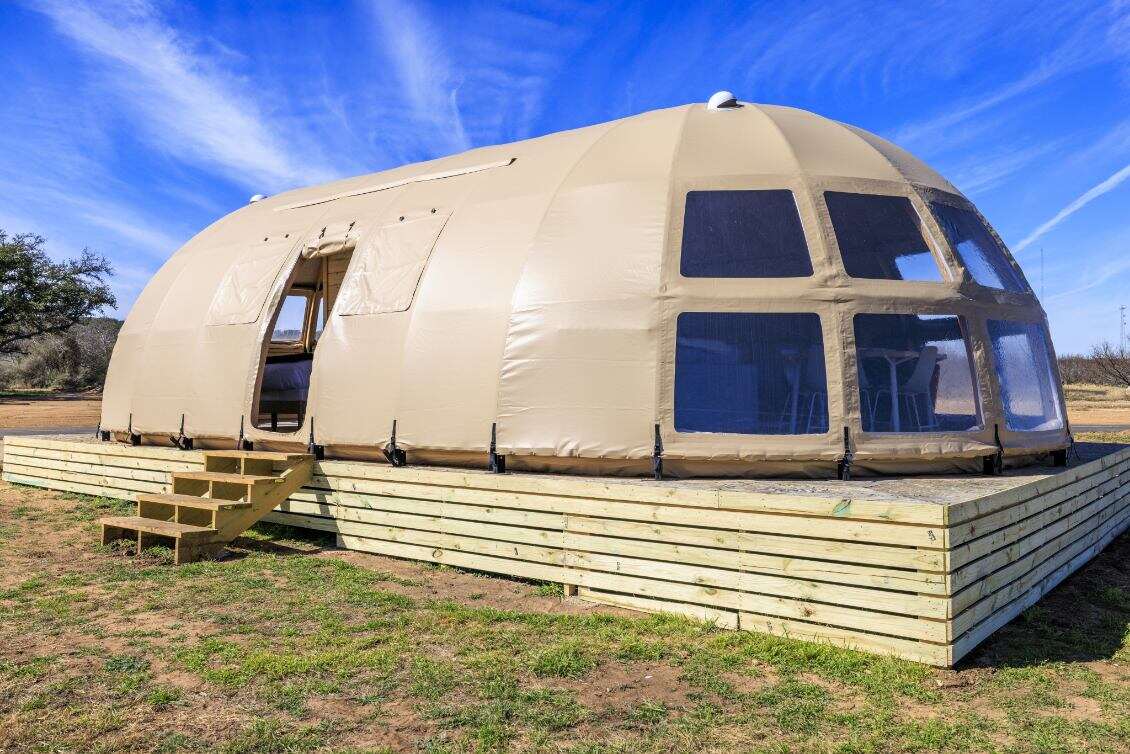 Alt text: "Spacious geodesic dome with porthole windows on a wooden platform, ideal for glamping or a luxury Airbnb experience. This large dome tent offers a stylish and sustainable living solution, perfect for a backyard dome or geodesic home setup."