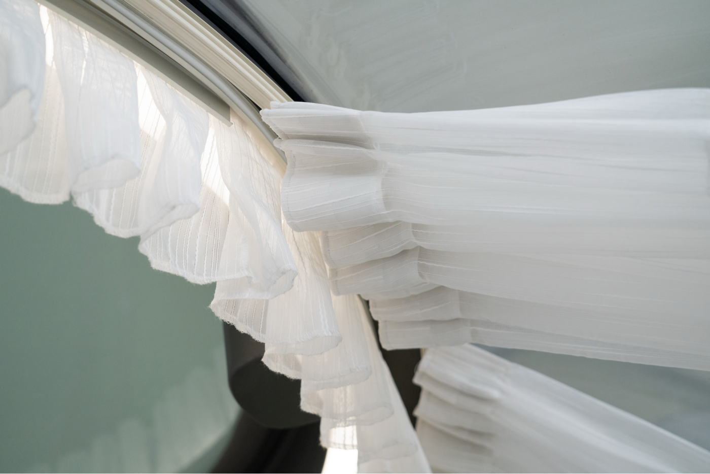 Alt text: "Close-up of white curtains inside a geodesic dome with porthole windows, showcasing the elegant interior design of a luxury glamping pod. Ideal for sustainable living and stylish outdoor accommodations."