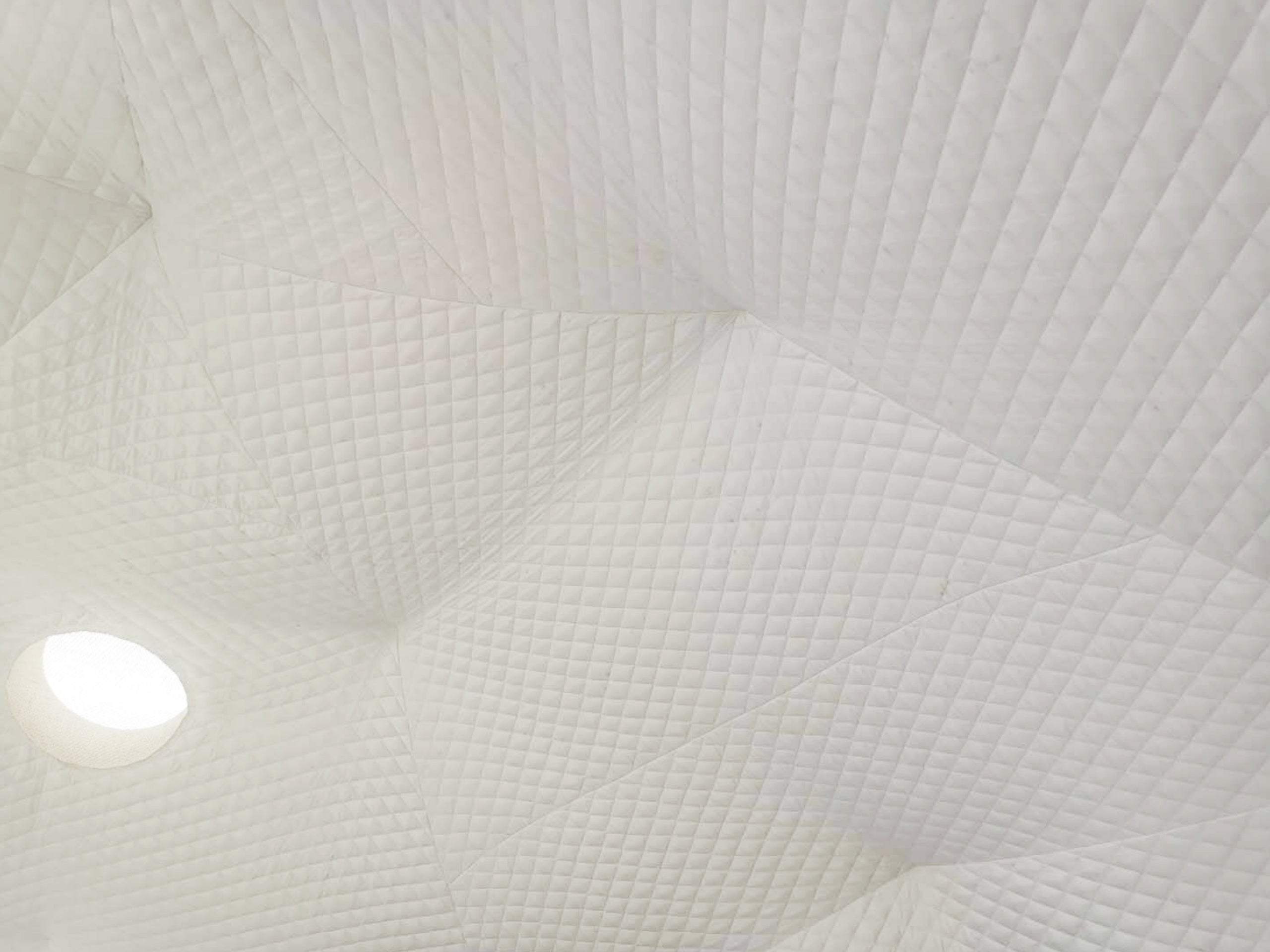 Alt text: "Interior view of a geodesic dome with quilted white fabric and a circular porthole window, showcasing the stylish and premium design of a glamping pod. Ideal for luxury Airbnb, backyard dome, or geodesic dome house kit."