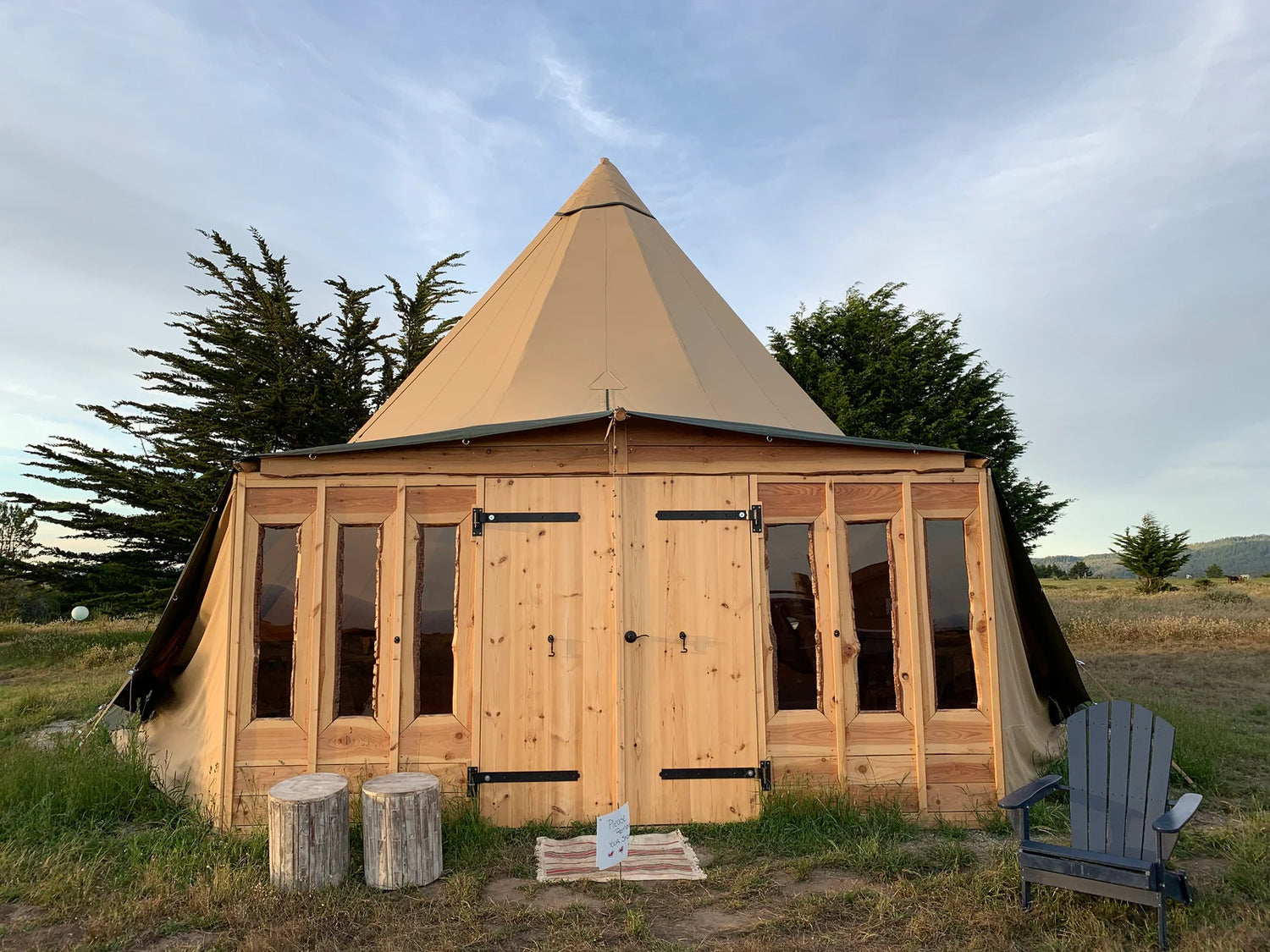 Alt text: "Stylish glamping teepee with wooden facade and porthole windows set in a scenic outdoor location, ideal for luxury camping or a unique backyard office. Explore premium geodesic dome and glamping solutions for sustainable living and creative spaces."