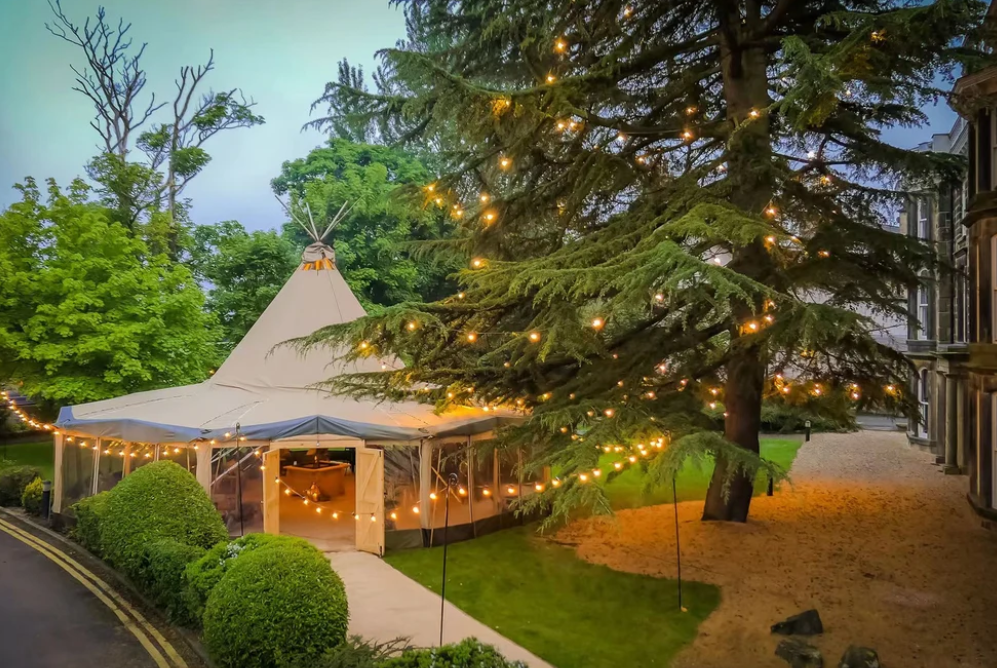 Alt text: "Elegant glamping setup featuring a large bell tent illuminated with string lights, surrounded by lush greenery. Ideal for luxury outdoor experiences, this stylish tent offers a premium glamping solution for those seeking a unique and comfortable stay."