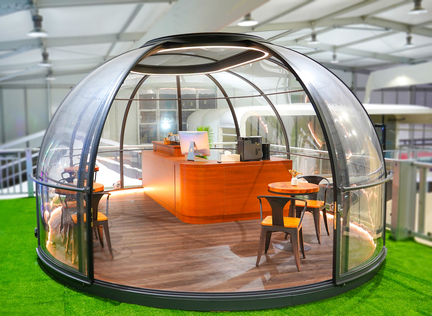 Alt text: "Modern geodesic dome with transparent walls, featuring a stylish interior setup with wooden furniture, suitable for glamping or as a backyard office. Ideal for those seeking luxury and sustainability in a dome home or outdoor dome solution."
