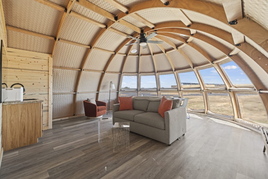 Interior view of a stylish geodesic dome home featuring a cozy living area with a gray sofa, red armchair, and modern decor. The dome&