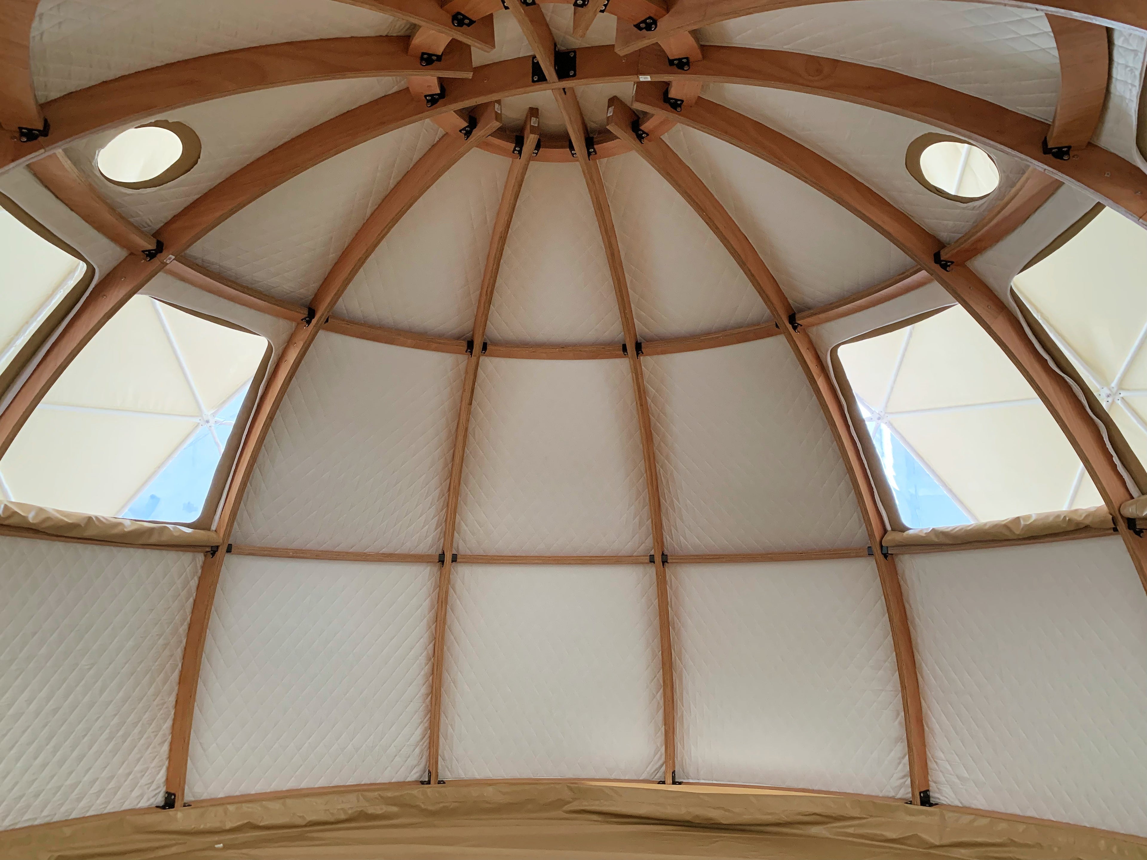 Interior view of a geodesic dome with wooden beams and porthole windows, showcasing the spacious and stylish design ideal for glamping solutions.