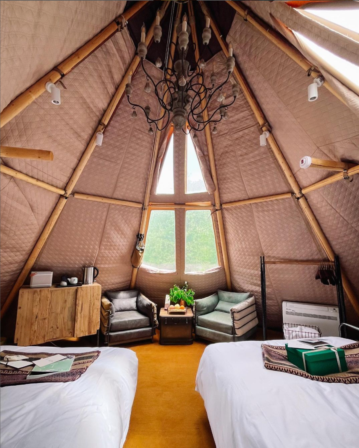 Interior view of a luxurious glamping dome featuring cozy seating, a wooden table, and a chandelier. The space is designed for comfort and style, ideal for a unique camping experience. Keywords: geodesic dome, glamping pod, luxury Airbnb, dome home.