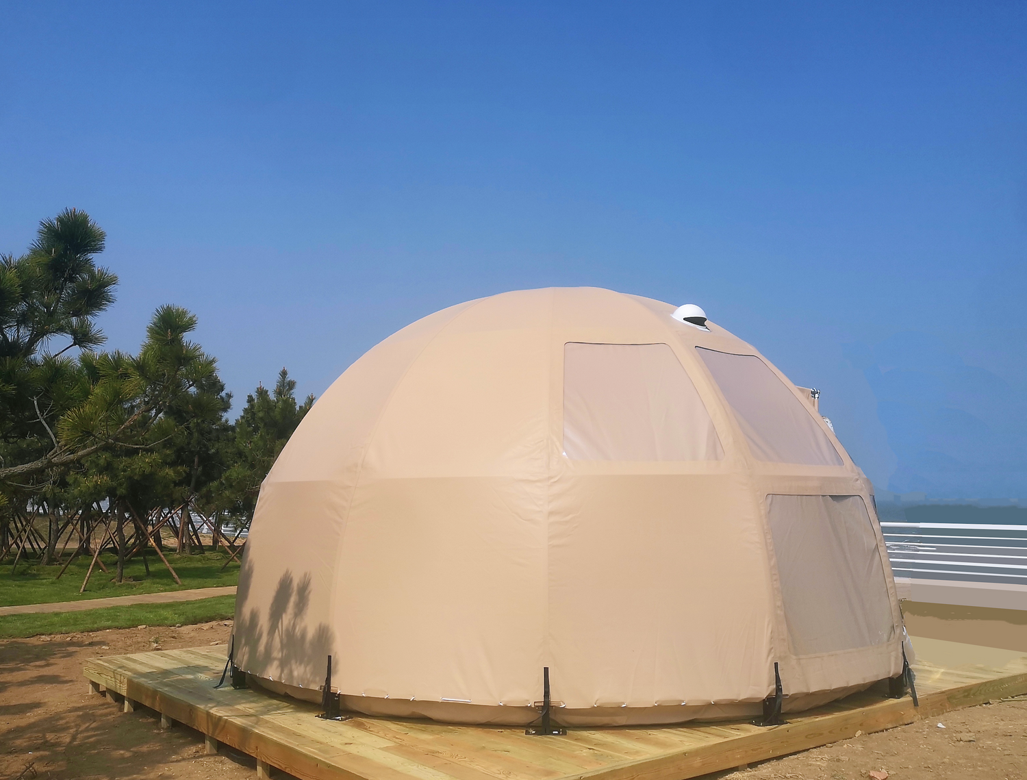 Alt text: &quot;Large beige geodesic dome tent with porthole windows set on a wooden platform, surrounded by trees, ideal for glamping or as a backyard dome office. High-quality, stylish, and cost-effective solution for sustainable living or luxury Airbnb experiences.&quot;