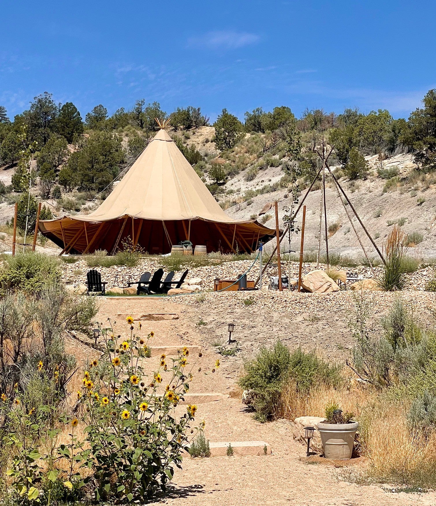 A spacious glamping teepee set in a scenic, natural landscape, ideal for sustainable living or creating a luxury Airbnb experience. The setup includes comfortable outdoor seating, surrounded by native plants and a clear blue sky, showcasing the company&