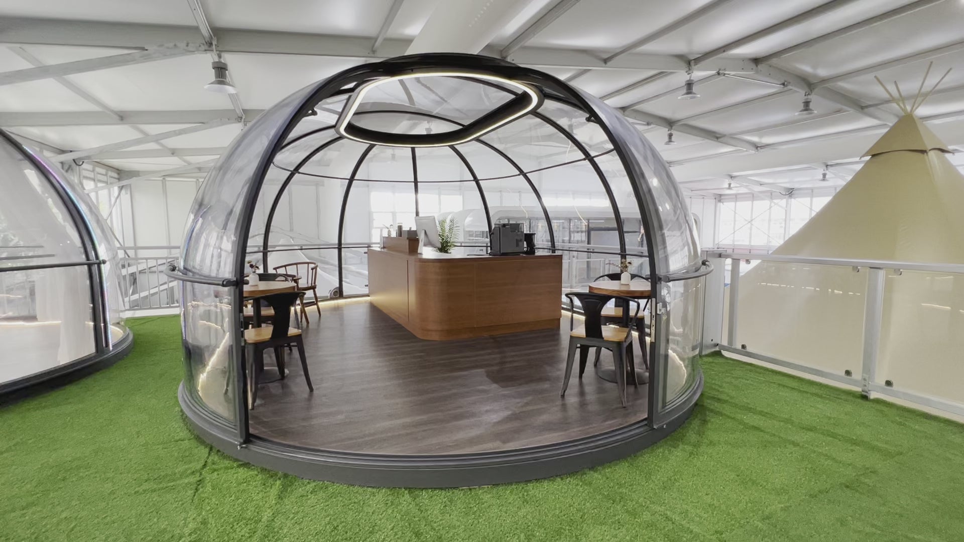 Alt text: "Modern geodesic dome with transparent walls, featuring a stylish interior setup with tables and chairs, ideal for glamping or a backyard office. The dome is situated on a green artificial grass surface, showcasing the company's high-quality glamping solutions."