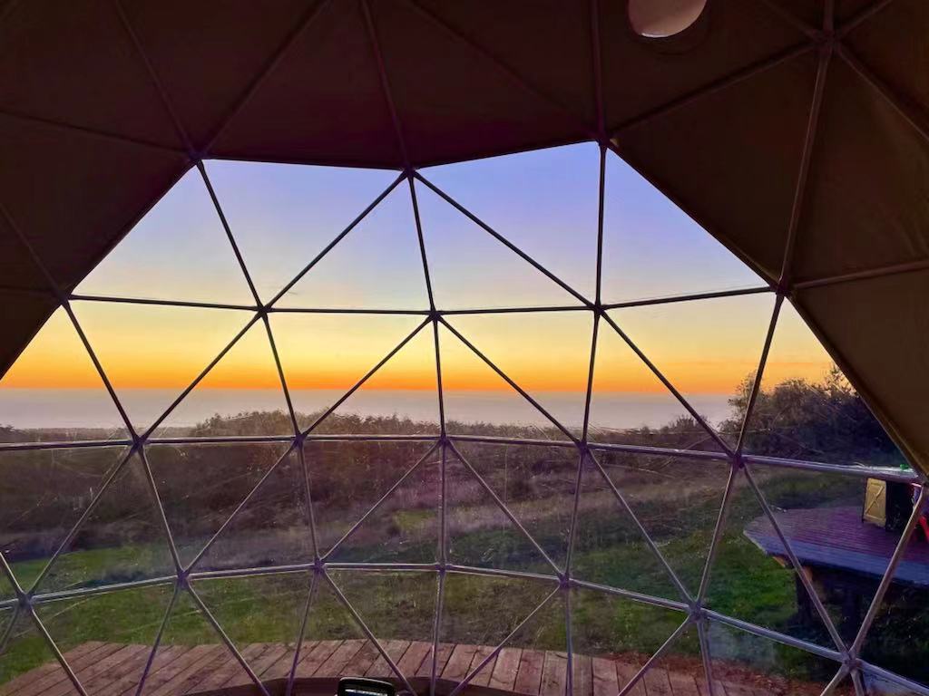 A stunning sunset view from inside a geodesic dome, showcasing the expansive landscape through the dome&