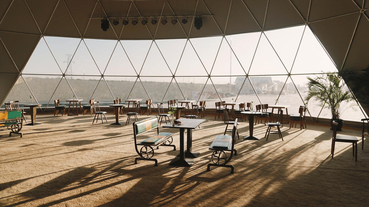 Alt text: &quot;Spacious interior of a geodesic dome with large porthole windows, featuring stylish seating and tables, ideal for luxury glamping or a unique event space. The dome&