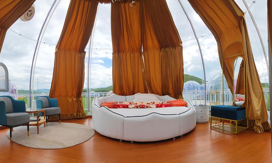 Interior view of a luxurious geodesic dome with a stylish round bed, elegant seating area, and large porthole windows, ideal for glamping or a unique backyard office.