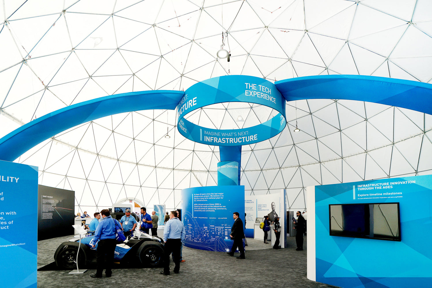 A modern exhibition inside a large geodesic dome showcasing innovative infrastructure solutions. The interior features informational displays and a sleek vehicle, highlighting the versatility of geodesic dome structures for events and exhibitions.