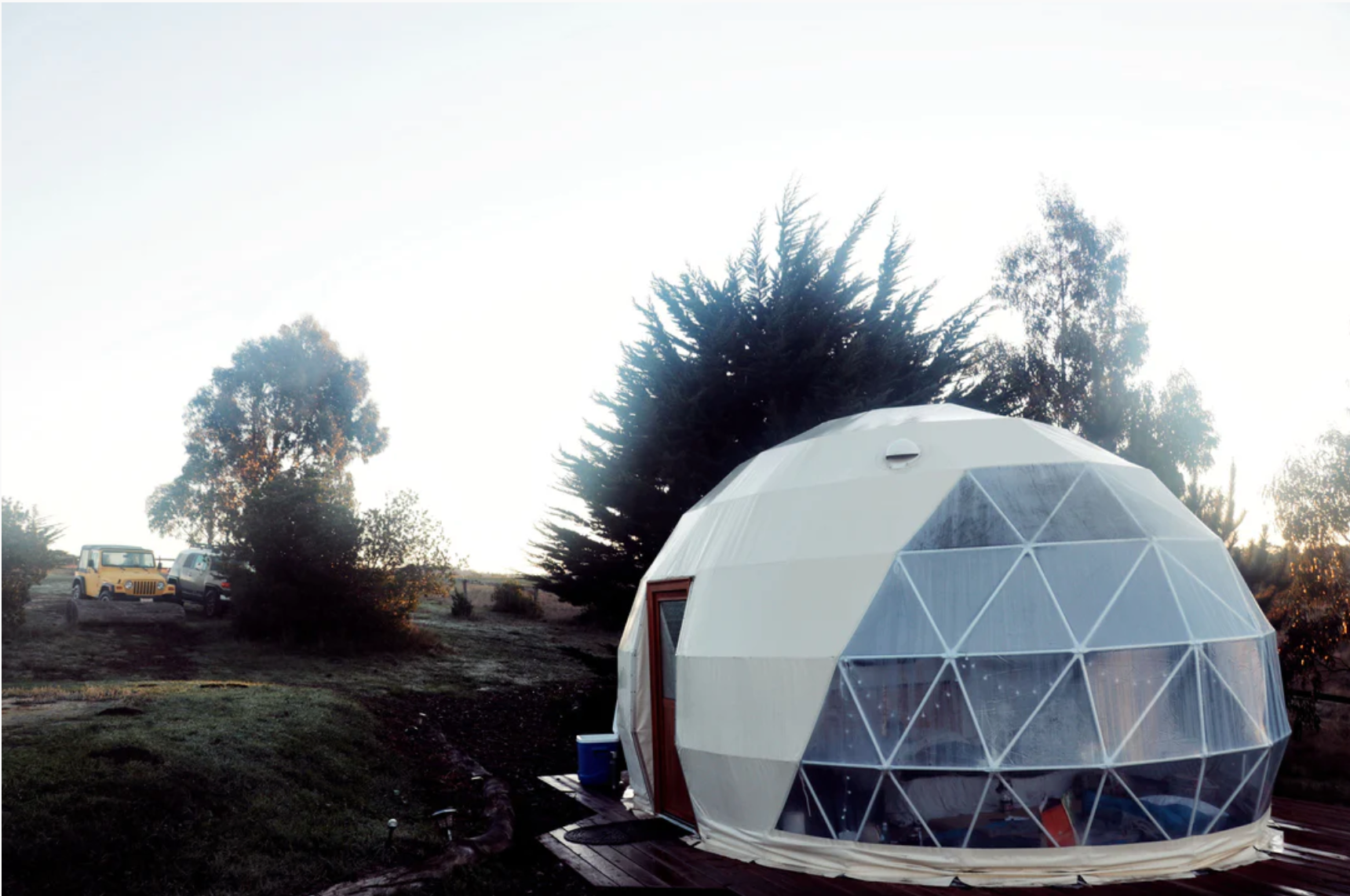 Alt text: &quot;Geodesic dome with porthole windows set in a scenic outdoor location, ideal for glamping or use as a backyard office. This large dome tent offers a stylish and sustainable living solution, perfect for those interested in luxury Airbnb experiences or creating a unique art studio space.&quot;