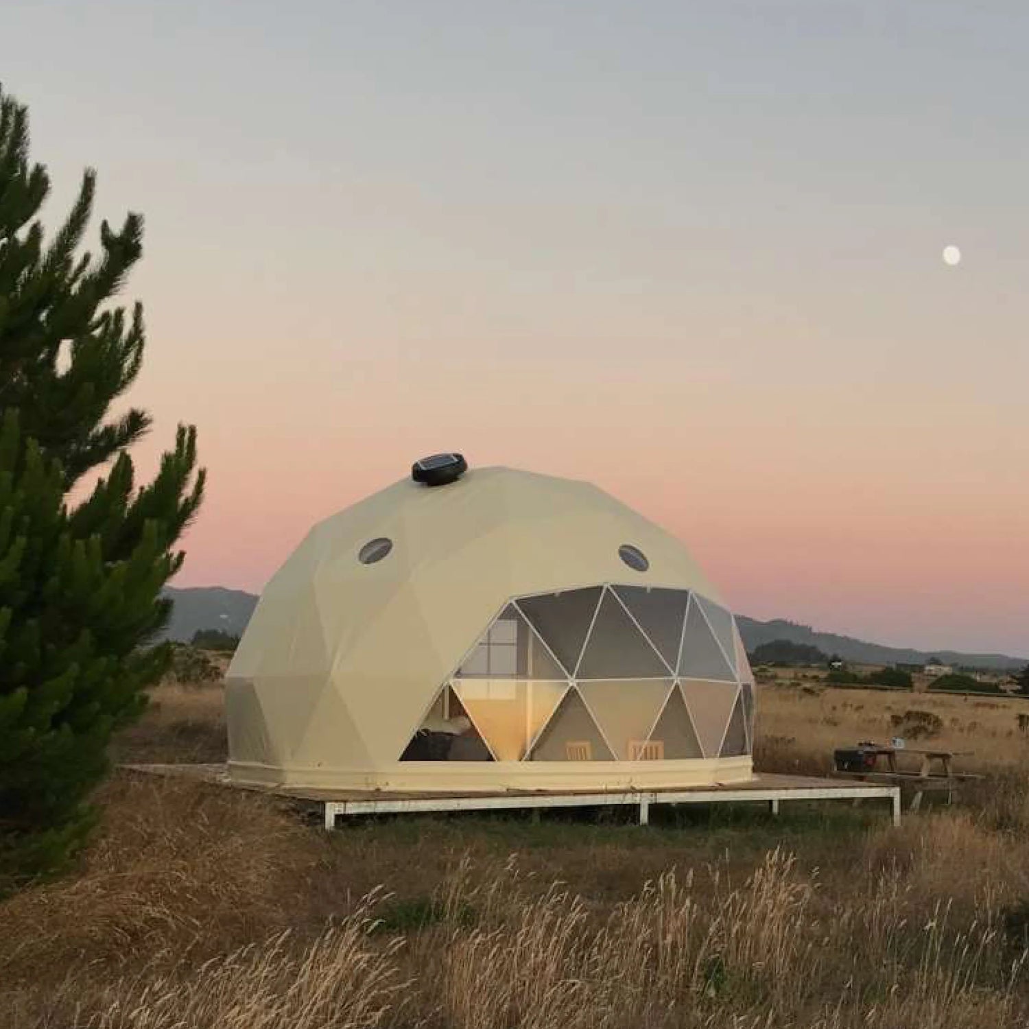 Alt text: &quot;Geodesic dome house with porthole windows set in a scenic outdoor location at sunset, showcasing a stylish and sustainable glamping solution. Ideal for luxury Airbnb, backyard dome, or art studio use.&quot;